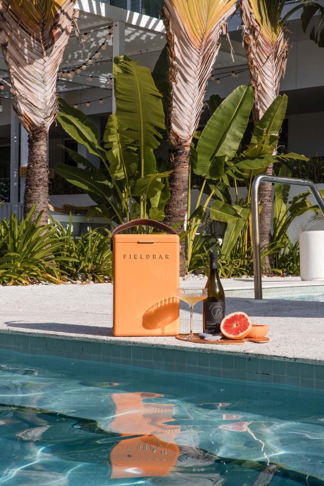 The pool deck at The Sarasota Modern — an orange cooler and a bottle at the tiled edge under the travellers' palms.