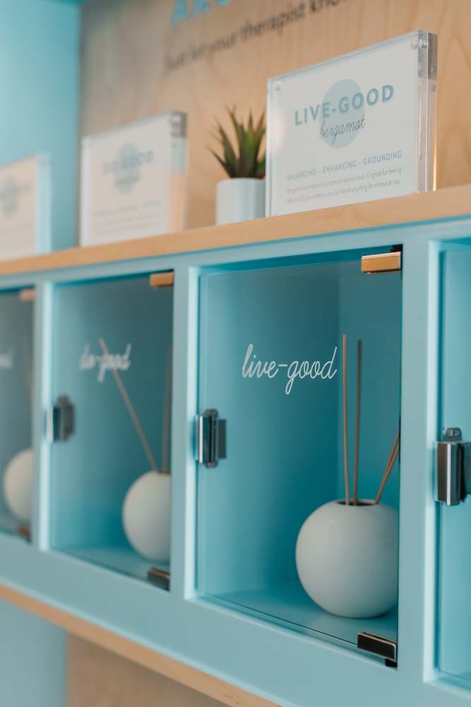 The aromatherapy wall at Squeeze — teal cabinets with live-good and do-good reed diffusers behind glass, and a card describing the bergamot blend.