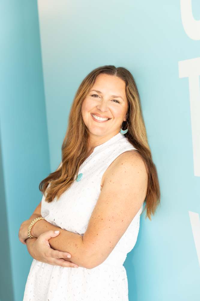 Sloane, the owner of Squeeze Sarasota, in a white eyelet dress against the studio's pale blue wall.