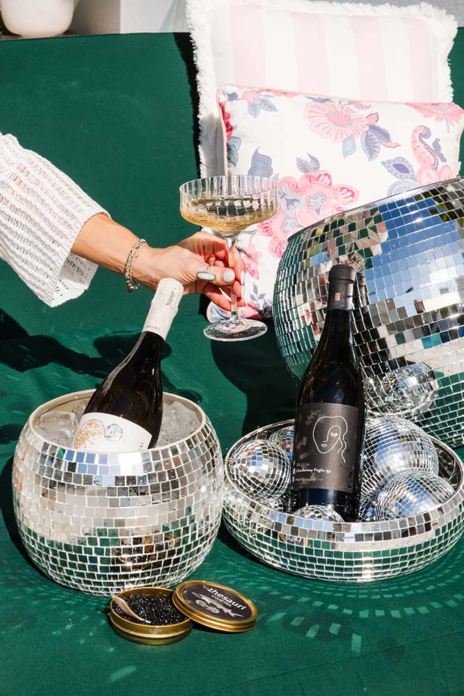 Pouring the extra-dry prosecco into a coupe over a pair of mirror-ball ice buckets on a green lounger.