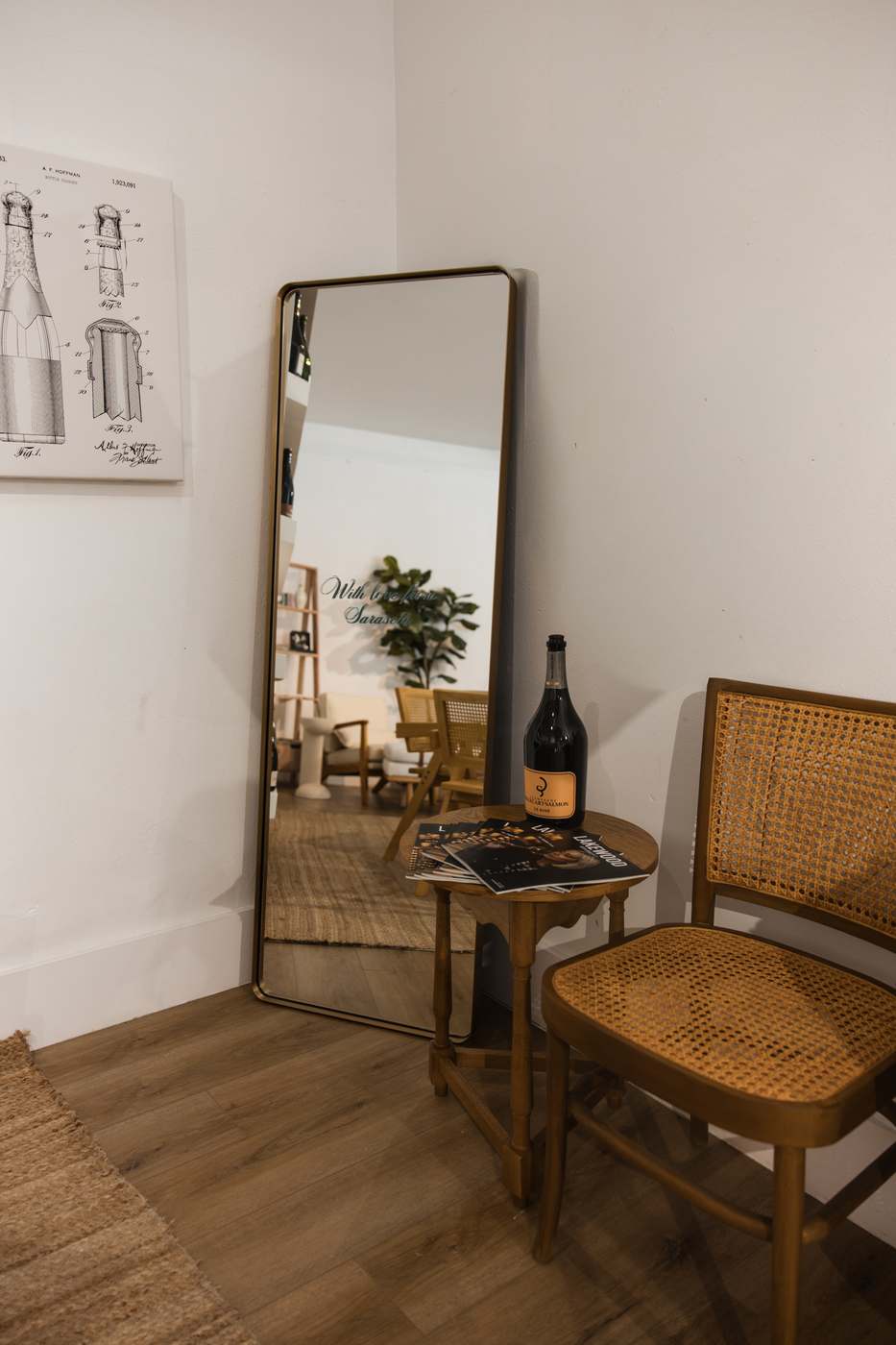 A quiet corner of Sarasota Wine Co. — a leaning mirror, a cane chair, and a bottle on a small round table.