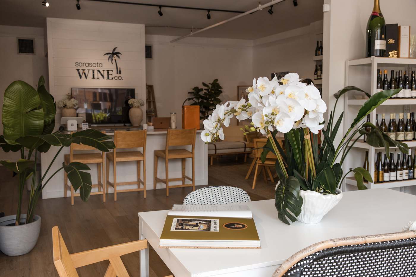 The tasting room at Sarasota Wine Co. — orchids on a white table, bar stools, wine shelves along the wall.